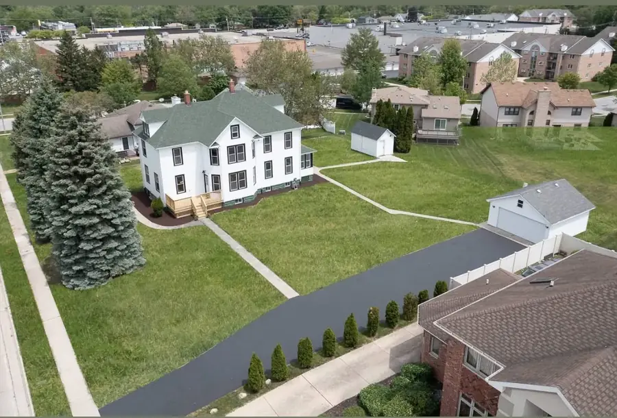 Aerial view of a renovated white home with green roof, new deck, and surrounding neighborhood